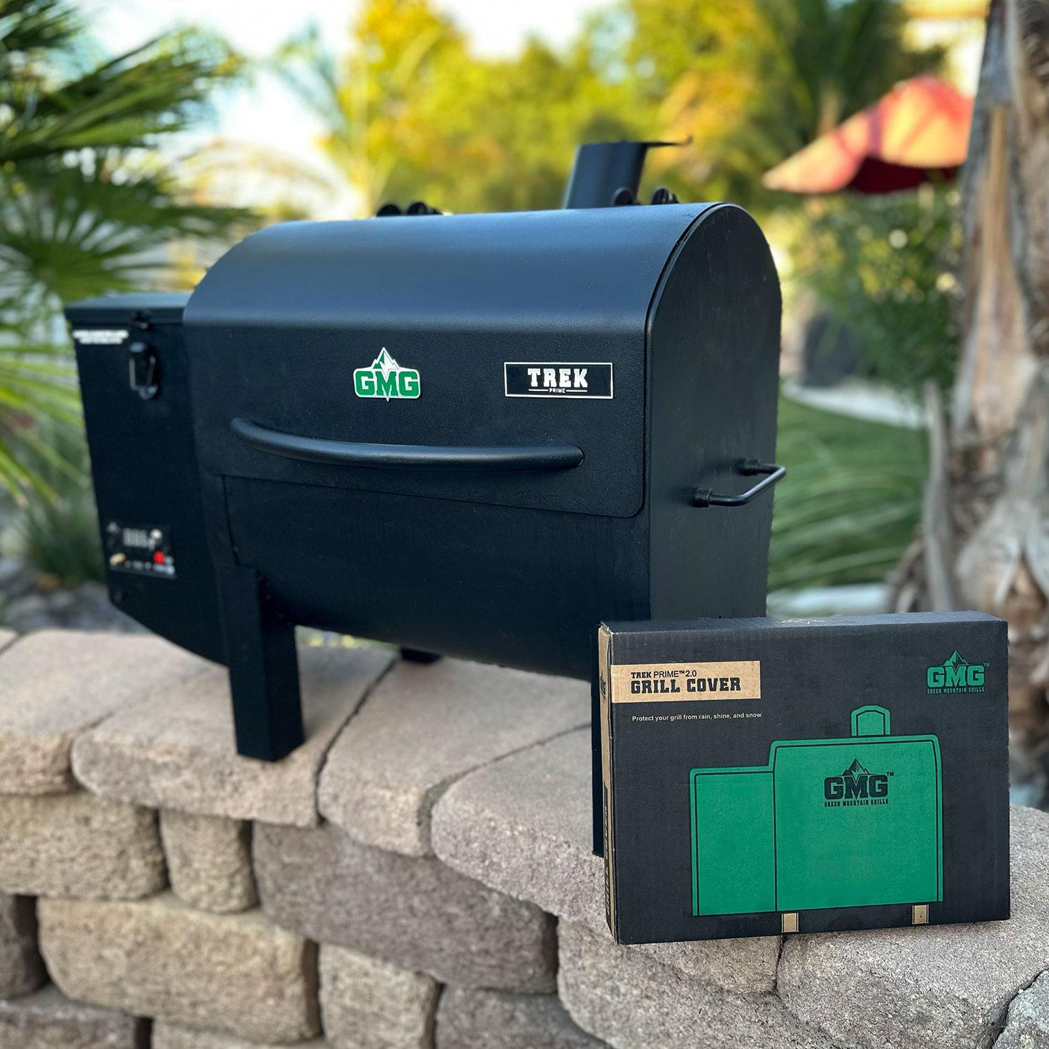 Portable Green Mountain Grills Trek smoker grill with GMG logo, accompanied by Trek Prime 2.0 grill cover, set against a natural outdoor background.